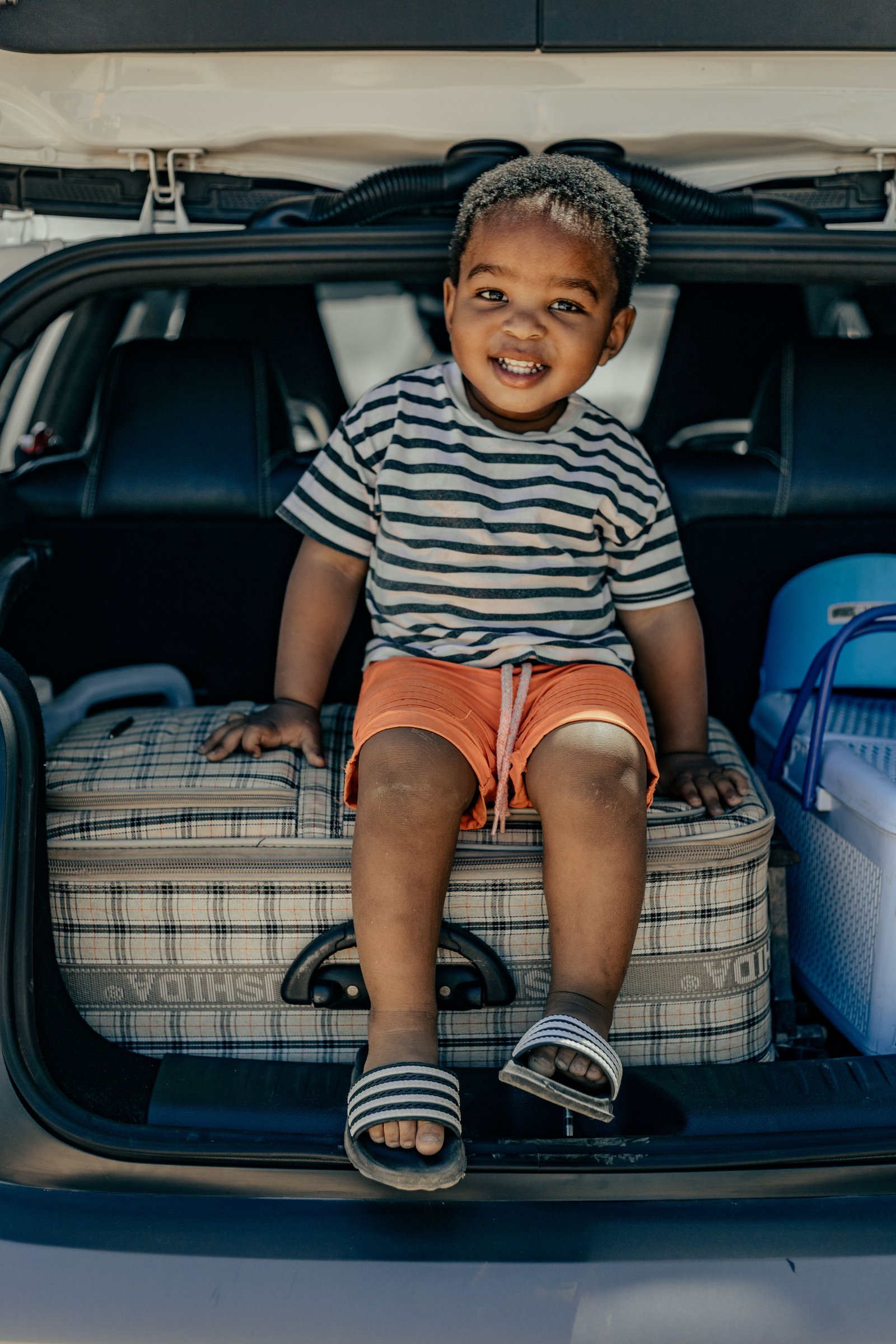 Tout-petit assis sur une valise dans le coffre familial avant le d&eacute;part